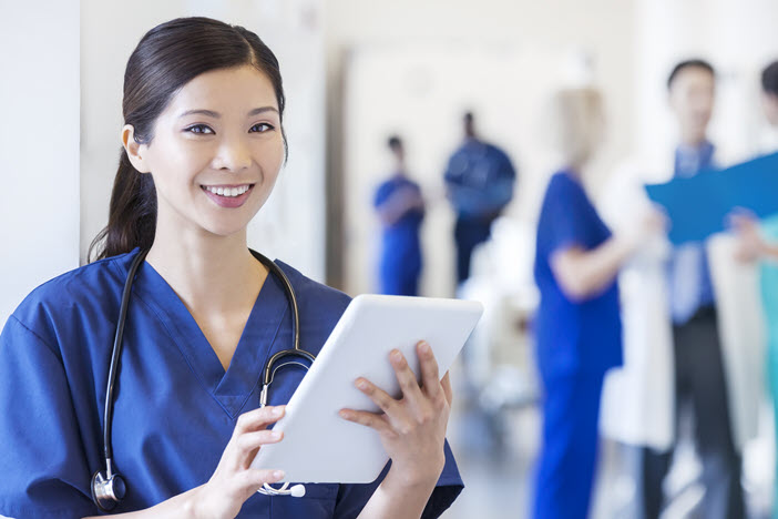 Smiling nurse, blue scrubs looking at a tablet