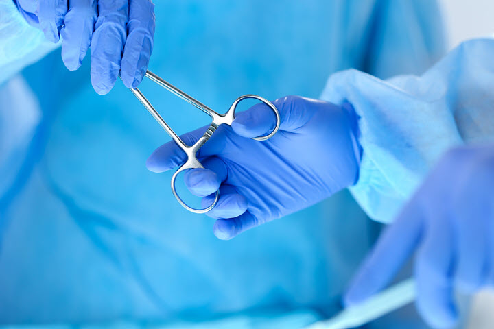 Two blue coated and gloved surgeons passing a clamp during surgery
